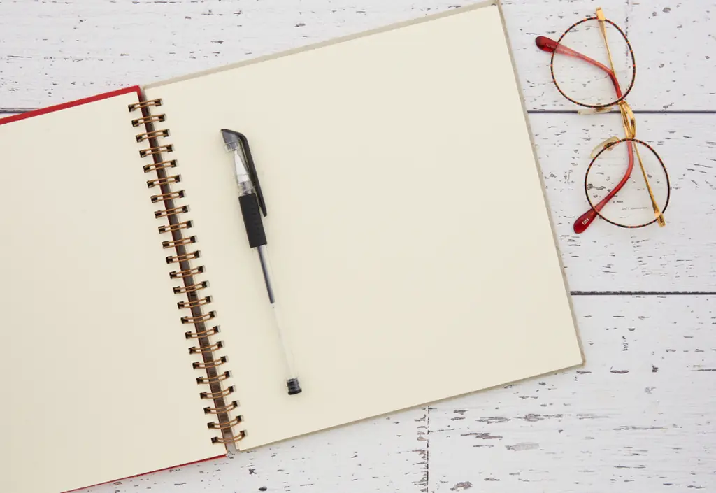 Image d’un carnet ouvert, d’un stylo et de lunettes, déposés sur une table claire